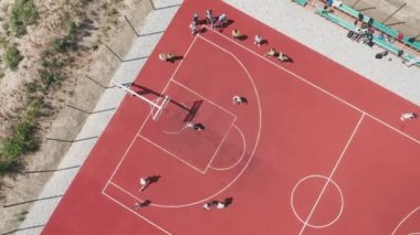 Aerial view of teens playing basketball on an outdoor public basketball court. Teenagers throwing a ball into a basketball basket at an open sports ground.