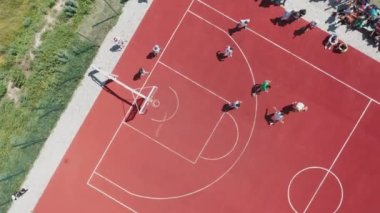 Aerial view of teenagers playing basketball on the outdoor summer basketball court. Teenagers are trying to throw the ball into the basketball basket on the outdoor sports ground.