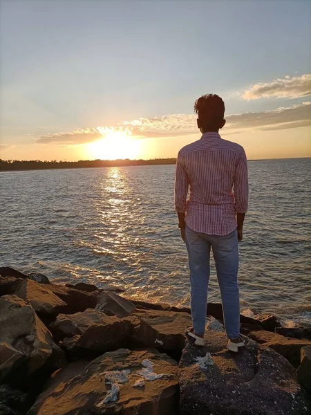 Büyük taşın üzerinde duran ve denizi gören bir adam.