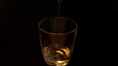 Pouring water into a clear glass close-up on black background