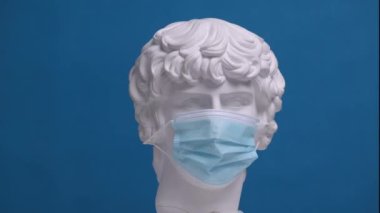 Yeni, temiz bir tıbbi maske Antinous 'un alçı büstünden masaya düştü..