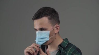Genç, beyaz erkek. Vape 'den çıkan buharı tıbbi maskeden çıkarıyor.