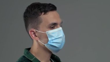Genç, beyaz erkek. Vape 'den çıkan buharı tıbbi maskeden çıkarıyor.