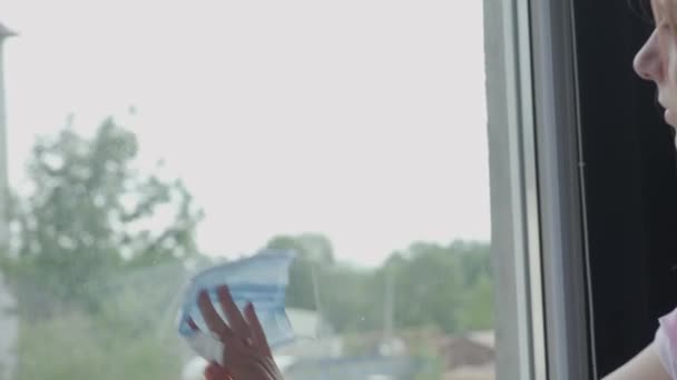 Flicka torkar ett smutsigt fönster med en ren medicinsk mask i stället för en servett Royaltyfri Stockvideo