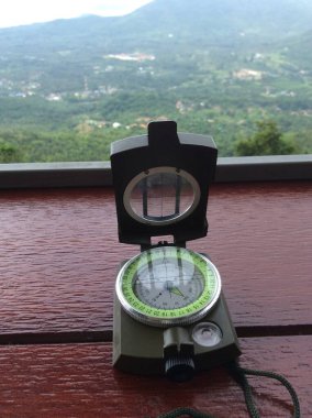 Tahta bir arka planda pusula ve dağ manzarası.