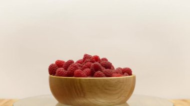 Rotating fresh, ripe raspberries in wooden bowl, on a white background