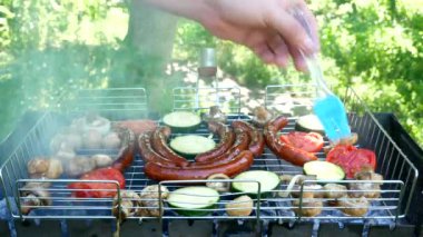 Kızarmış sosis, sebze ve mantarlar pişirme fırçasıyla kaplıdır. Açık havada ızgara sosis. B-B-Q. Yemek pikniği ve kamp kavramı. Yakın plan.