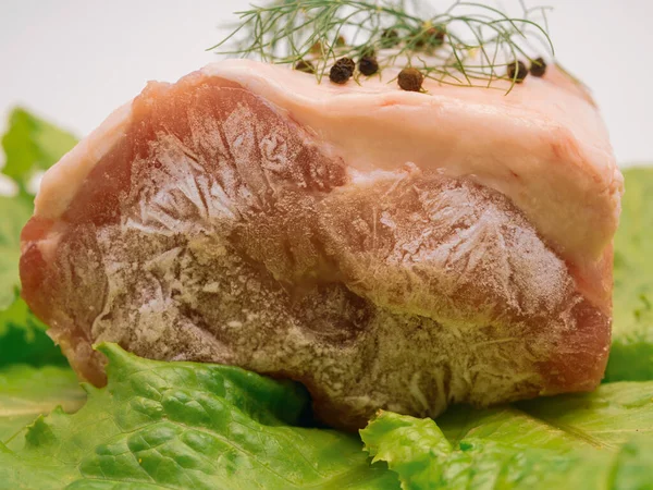 Piece of frozen meat, from which blows frosty freshness and cold. The meat lies on the leaves of fresh, green lettuce. Close-up