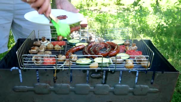 Grilled fried, juicy sausages are placed on a white plate. Roasting on the grill. Fried sausages and vegetable on the grill outdoors. B-B-Q. Fried food is fried and smoked on charcoal grills. It turns