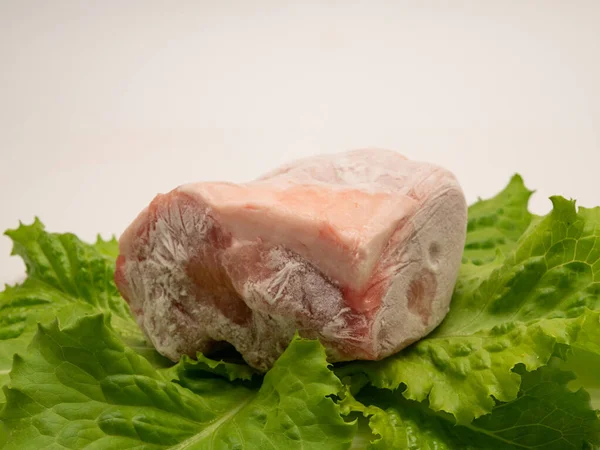 Piece of frozen meat, from which blows frosty freshness and cold. The meat lies on the leaves of fresh, green lettuce. Place for your text. Close-up