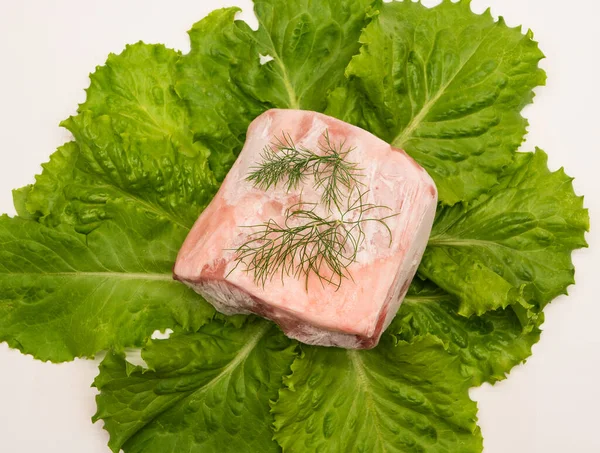 Piece of frozen meat, from which blows frosty freshness and cold. The meat lies on the leaves of fresh, green lettuce. Top view. Close-up