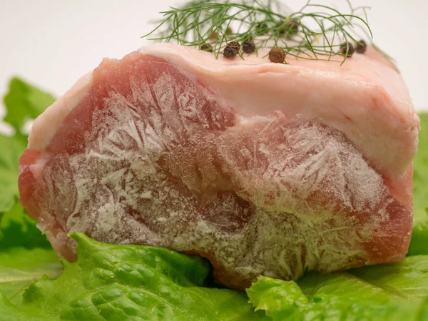 Piece of frozen meat, from which blows frosty freshness and cold. The meat lies on the leaves of fresh, green lettuce. Close-up