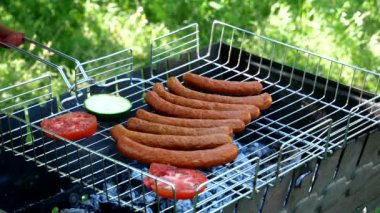 Roasting vegetables on the grill. The cook puts tomatoes, zucchini on the grill. Fried sausages on the grill outdoors. B-B-Q. Fried food is fried and smoked on charcoal grills. It turns out a grill with delicious tasty sausages and vegetables. 