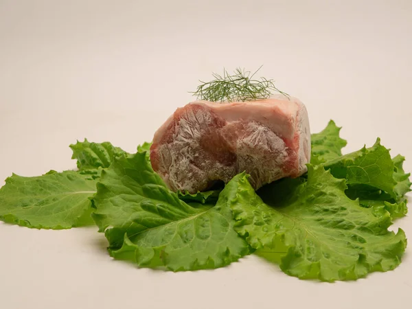 Piece of frozen meat, from which blows frosty freshness and cold. The meat lies on the leaves of fresh, green lettuce. Close-up