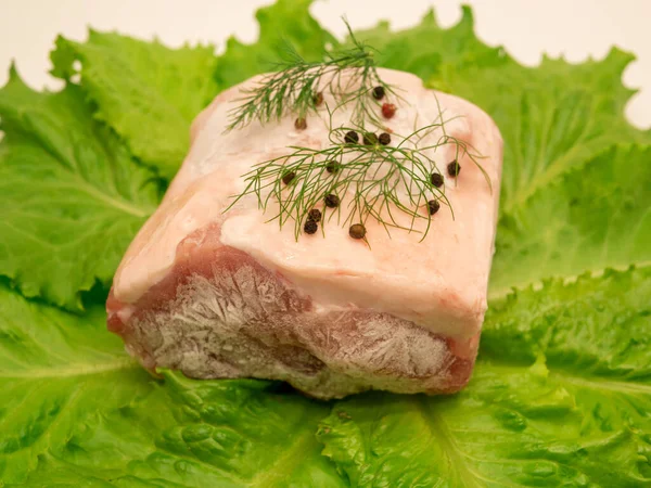 Piece of frozen meat, from which blows frosty freshness and cold. The meat lies on the leaves of fresh, green lettuce. Close-up