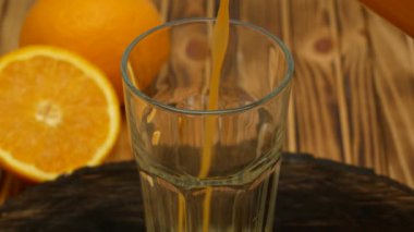 Fresh orange juice is poured into a transparent glass on a wooden background. Ripe oranges around a glass with juice. Close up.