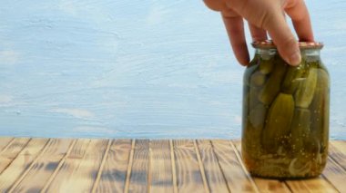 Pickled cucumbers in glass jars. Jars with pickled cucumbers are placed on a wooden table on a blue background. Pickling cucumbers at home. Vegetable harvest conservation. Preservations, conservation.