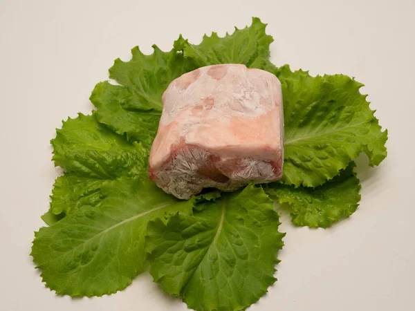 Piece of frozen meat, from which blows frosty freshness and cold. The meat lies on the leaves of fresh, green lettuce. Close-up