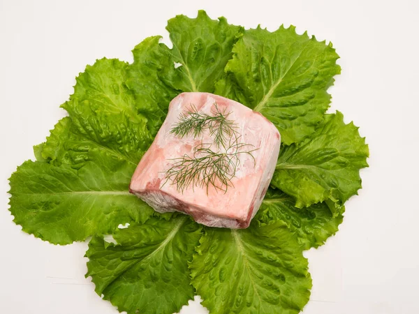 Piece of frozen meat, from which blows frosty freshness and cold. The meat lies on the leaves of fresh, green lettuce. Top view. Close-up