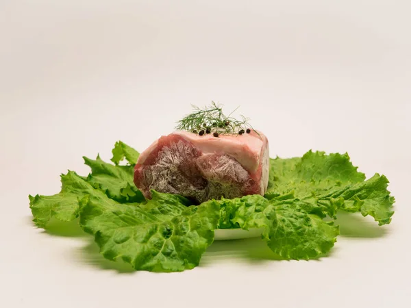 Piece of frozen meat, from which blows frosty freshness and cold. The meat lies on the leaves of fresh, green lettuce. Close-up