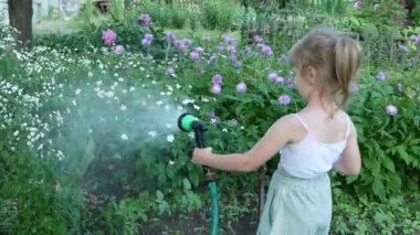 Little girl child holds a hose with a sprayer and watered the plants in the garden.
