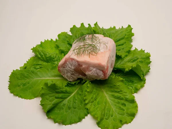 Piece of frozen meat, from which blows frosty freshness and cold. The meat lies on the leaves of fresh, green lettuce. Close-up