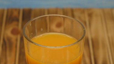 Rotation of orange juice in a glass. Cocktail with orange juice on a wooden background. Close up.
