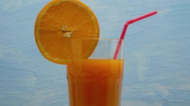 Rotation of orange juice in a glass. Cocktail with orange juice on a blue background. Close up.