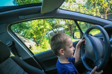 Dört yaşında bir çocuk direksiyonda oturur ve araba sürüyormuş gibi yapar.