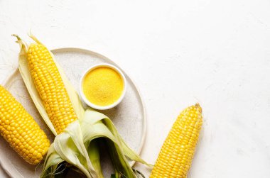 Üç mısır koçanı ve bir kase mısır unu, beyaz arka planda bir tabakta.. 