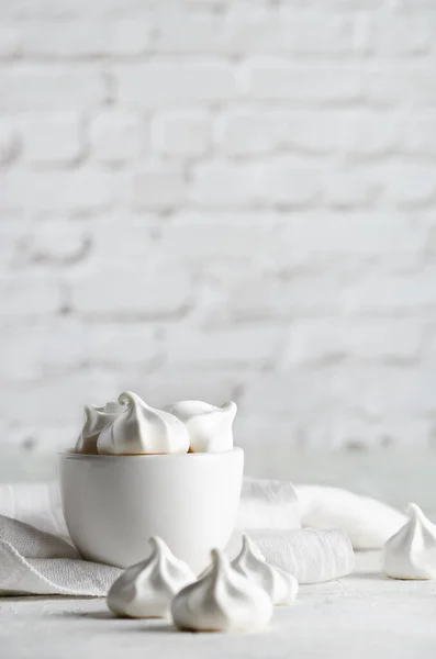 White meringue cookies in a white bowl with a white napkin, on white background.
