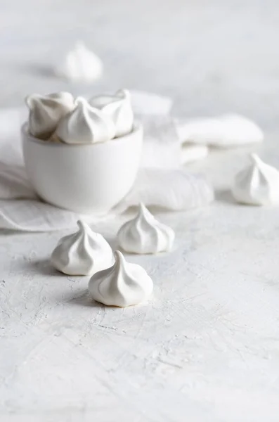 White meringue cookies in a white bowl with a white napkin, on white background. 
