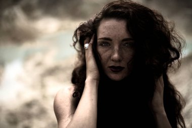 Kızıl kıvırcık saçlı ve kameraya bakan genç bir kadının portresi. Kızıl saçlı, çilli kızın yüzünü kapat..