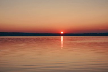 Gün batımının görkemli manzarası. Güneş bir dağın arkasında batıyor. Önünde deniz var.. 