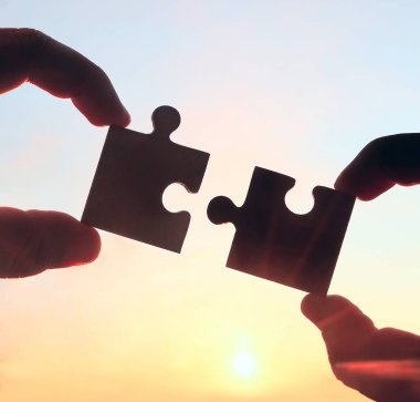 Gökyüzü arka planında yapboz parçaları olan eller.  