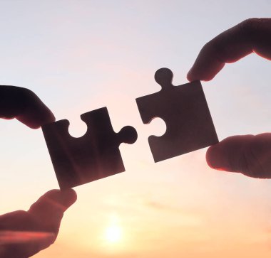 Gökyüzü arka planında yapboz parçaları olan eller.  