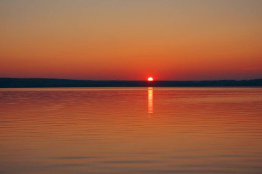 Gün batımının görkemli manzarası. Güneş bir dağın arkasında batıyor. Önünde deniz var.. 