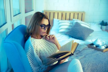 Boş zaman. Kız kitap okuyor, pencereye karşı koltukta oturuyor.