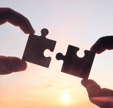 Gökyüzü arka planında yapboz parçaları olan eller.  