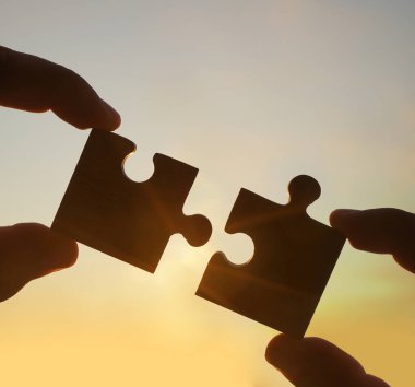 Gökyüzü arka planında yapboz parçaları olan eller.  