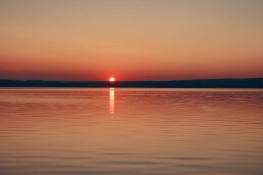 Gün batımının görkemli manzarası. Güneş bir dağın arkasında batıyor. Önünde deniz var.. 