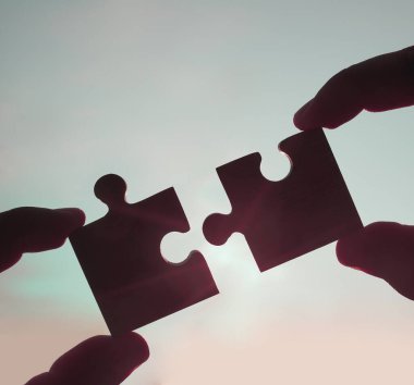 Gökyüzü arka planında yapboz parçaları olan eller.  