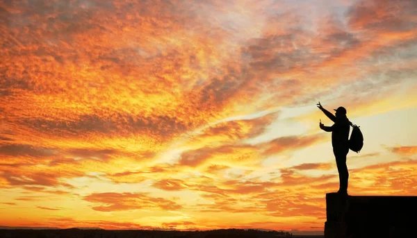Gün batımında dağda duran turist silueti. İşaret parmağının yönünü gösterir