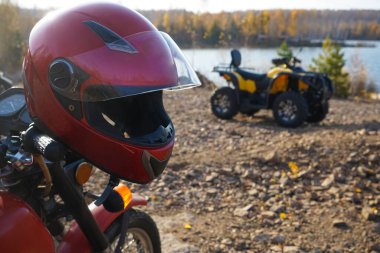 Motosikletin gidonundaki miğfer bir ATV, göl ve sonbahar ormanının arka planına karşı.