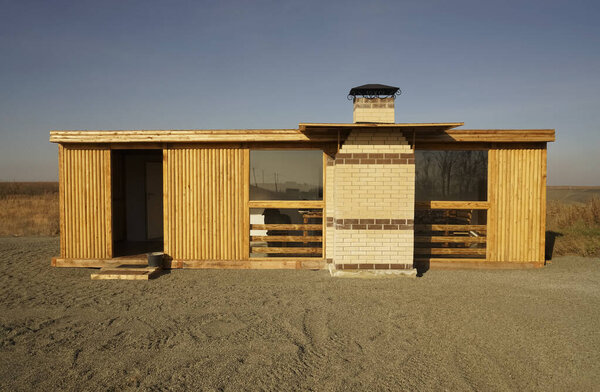 Front of the Modern villa with a breakstone and blue sky. The house has a small stones on ground. wooden house and glasses windows. 