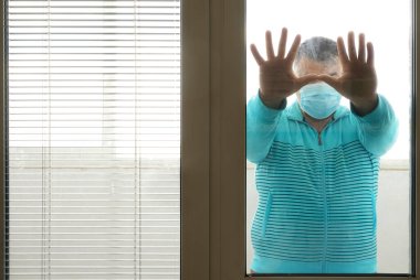 Kendini izole eden tıbbi maskeli bir adam bir evin penceresinden sokağa bakıyor. Tıbbi maskeli adam evde kalıyor. Evde kendi kendini izole ediyor. Karantinaya alınmış, toplumdan soyutlanmış..