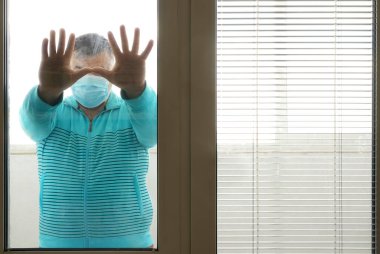 Kendini izole eden tıbbi maskeli bir adam bir evin penceresinden sokağa bakıyor. Tıbbi maskeli adam evde kalıyor. Evde kendi kendini izole ediyor. Karantinaya alınmış, toplumdan soyutlanmış..