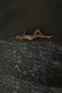 Kumsalda, siyah bir mayo içinde, bronzlaşmış bir vücudu, uzun sarı saçları ve muhteşem göğüsleri olan güzel seksi bir manken.. 