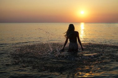Dertsiz genç bir kadının gün batımında denize koşması.