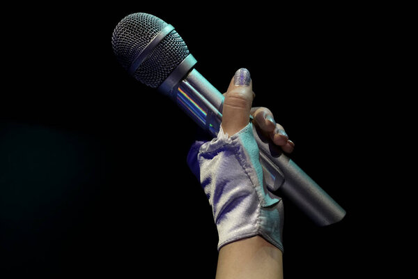 A woman in a leather glove holding a big silver wireless microphone for singing isolated on black  background. Rock star with beautiful manicure singing. no face. 